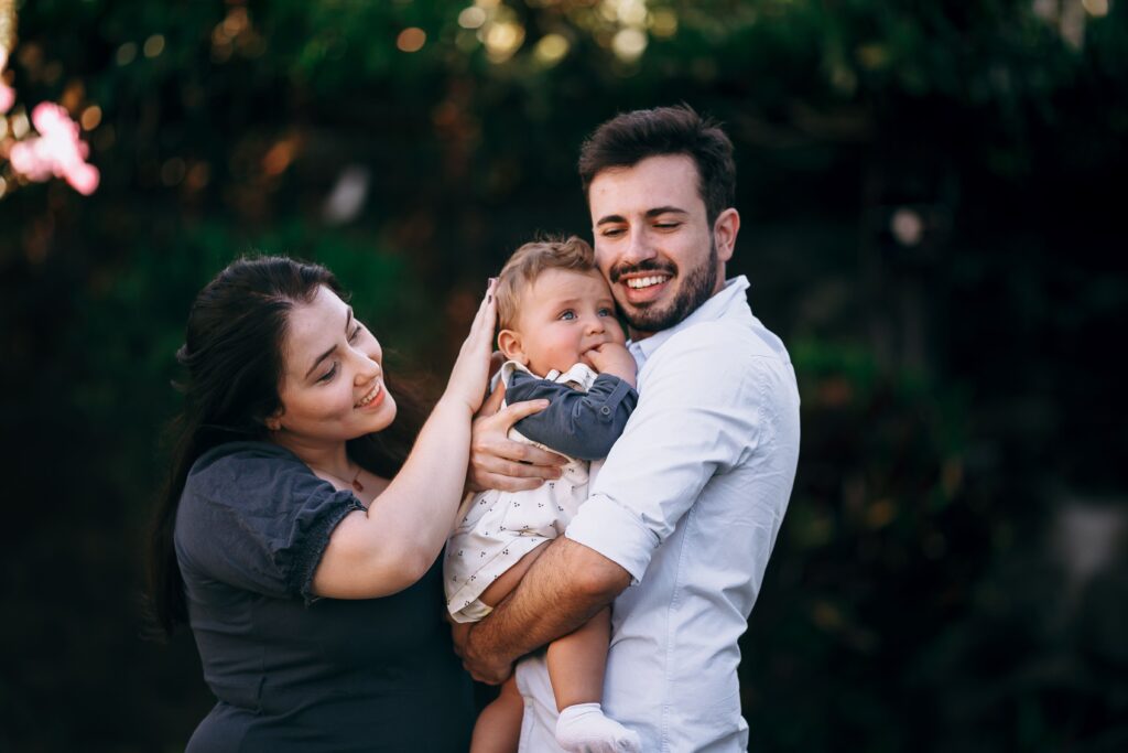 pexels photo 27177001 27177001 A joyful family with parents embracing their baby in a sunny park setting.